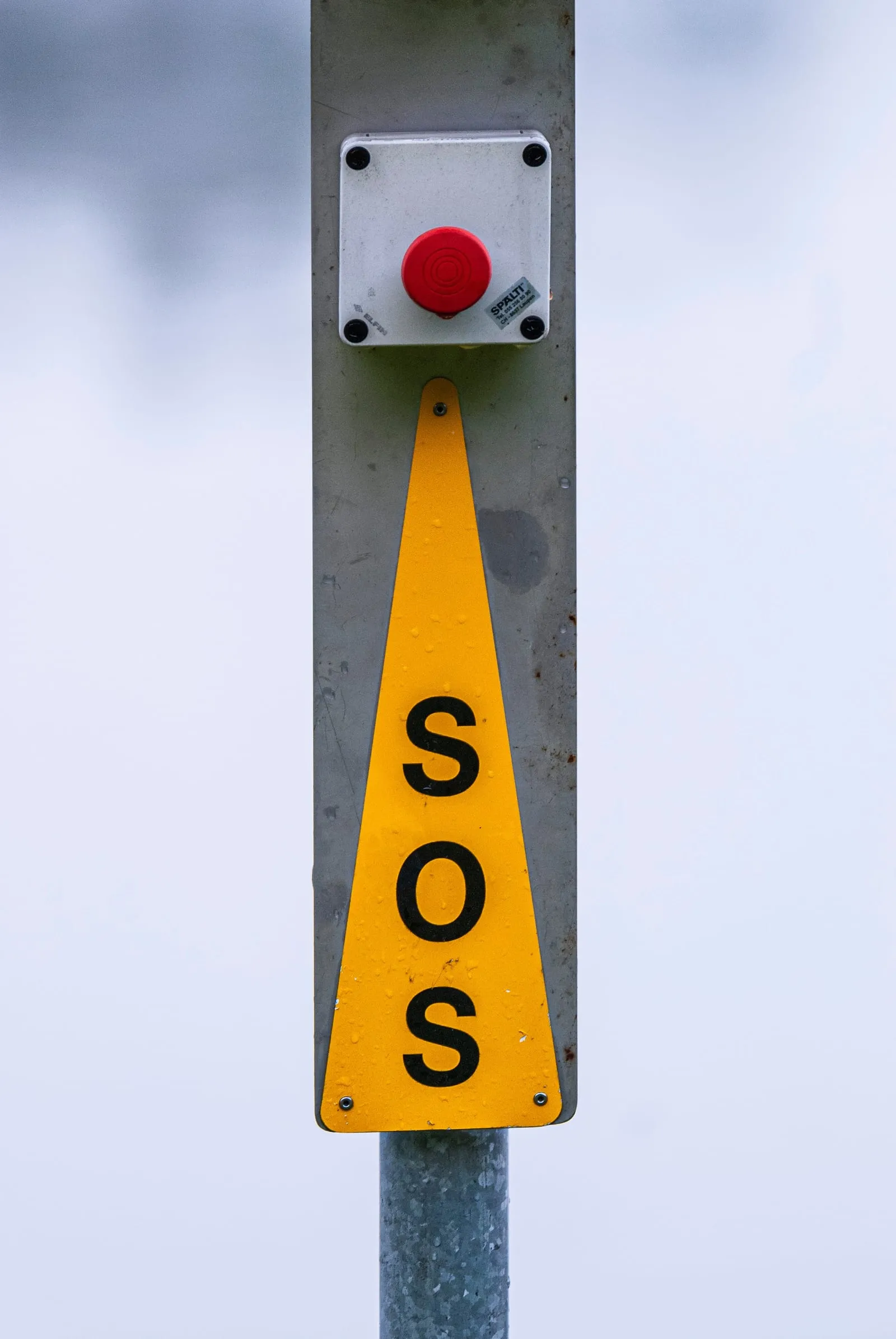 Yellow SOS emergency sign with a red call button mounted on a pole